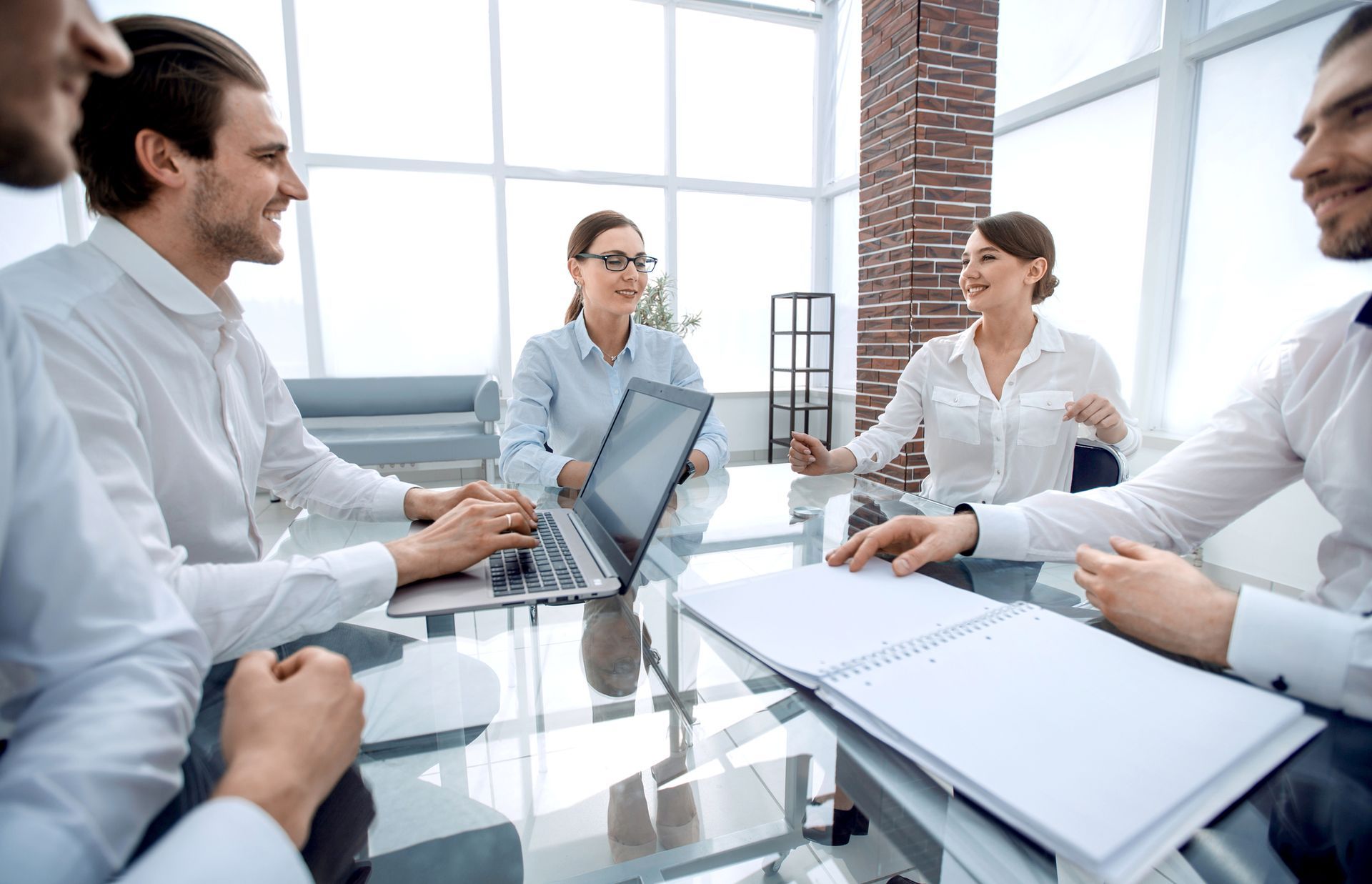 A group of people are sitting around a table with laptops.