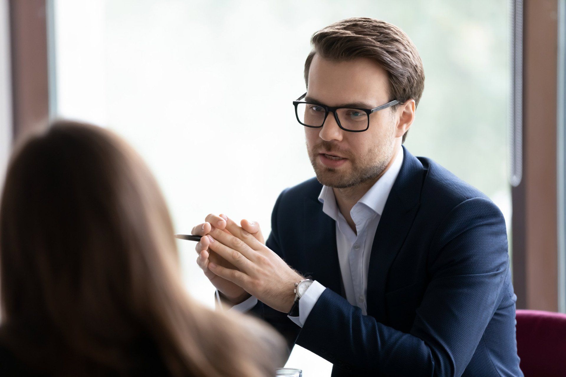 A man in a suit and glasses is sitting at a table talking to a woman.