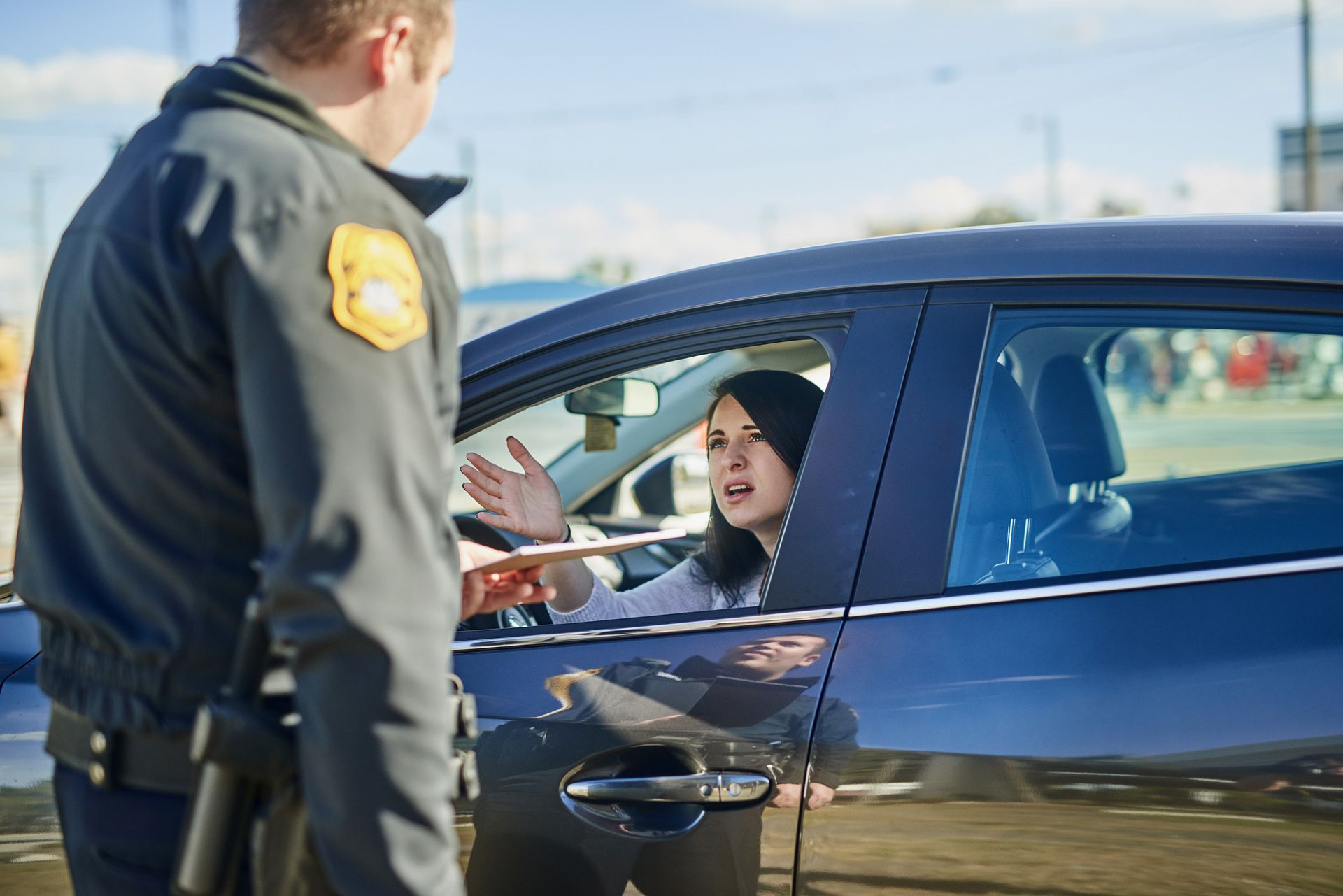 Police officer talking to a frustrated woman in a car, outdoors.