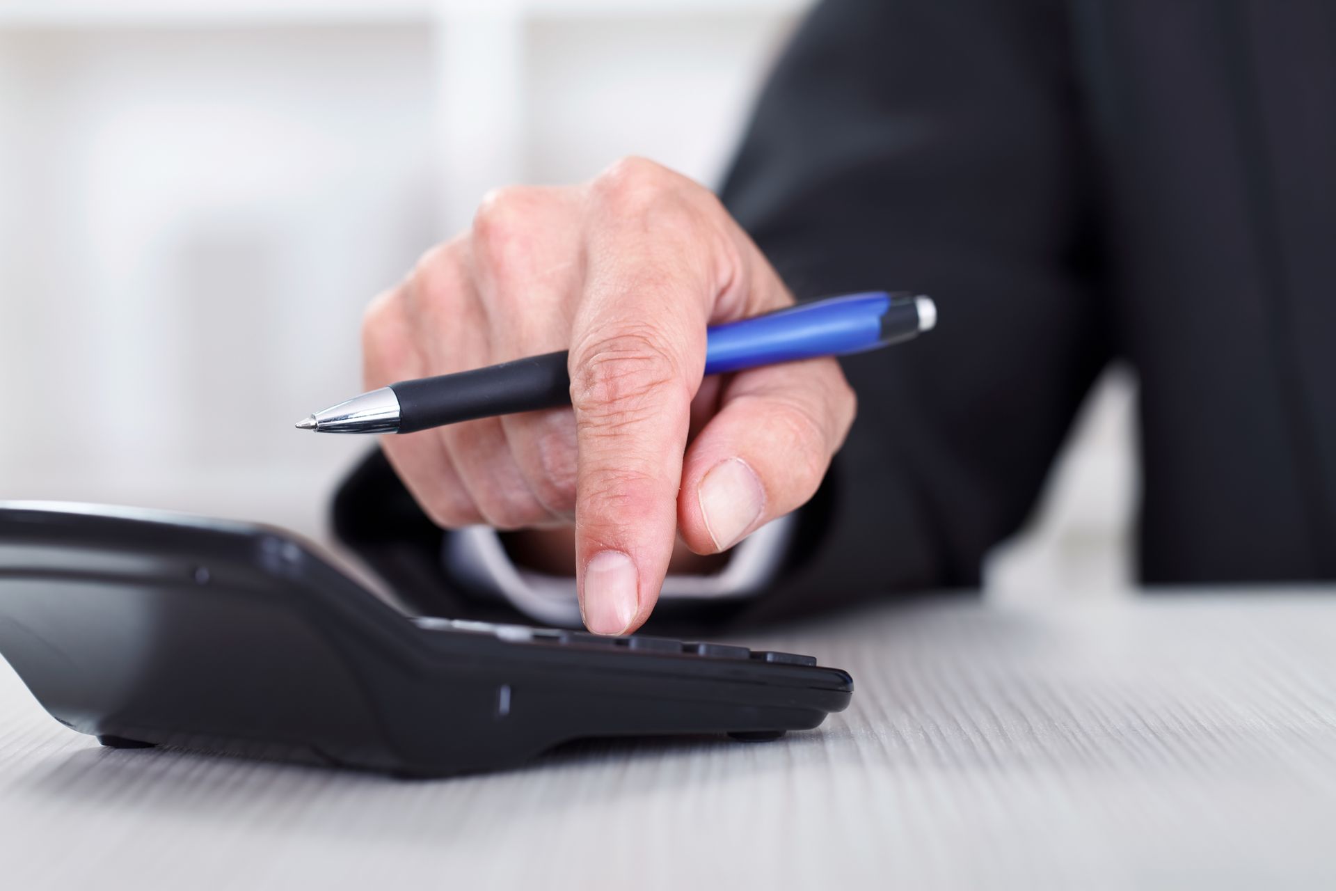 A person is using a calculator while holding a pen.