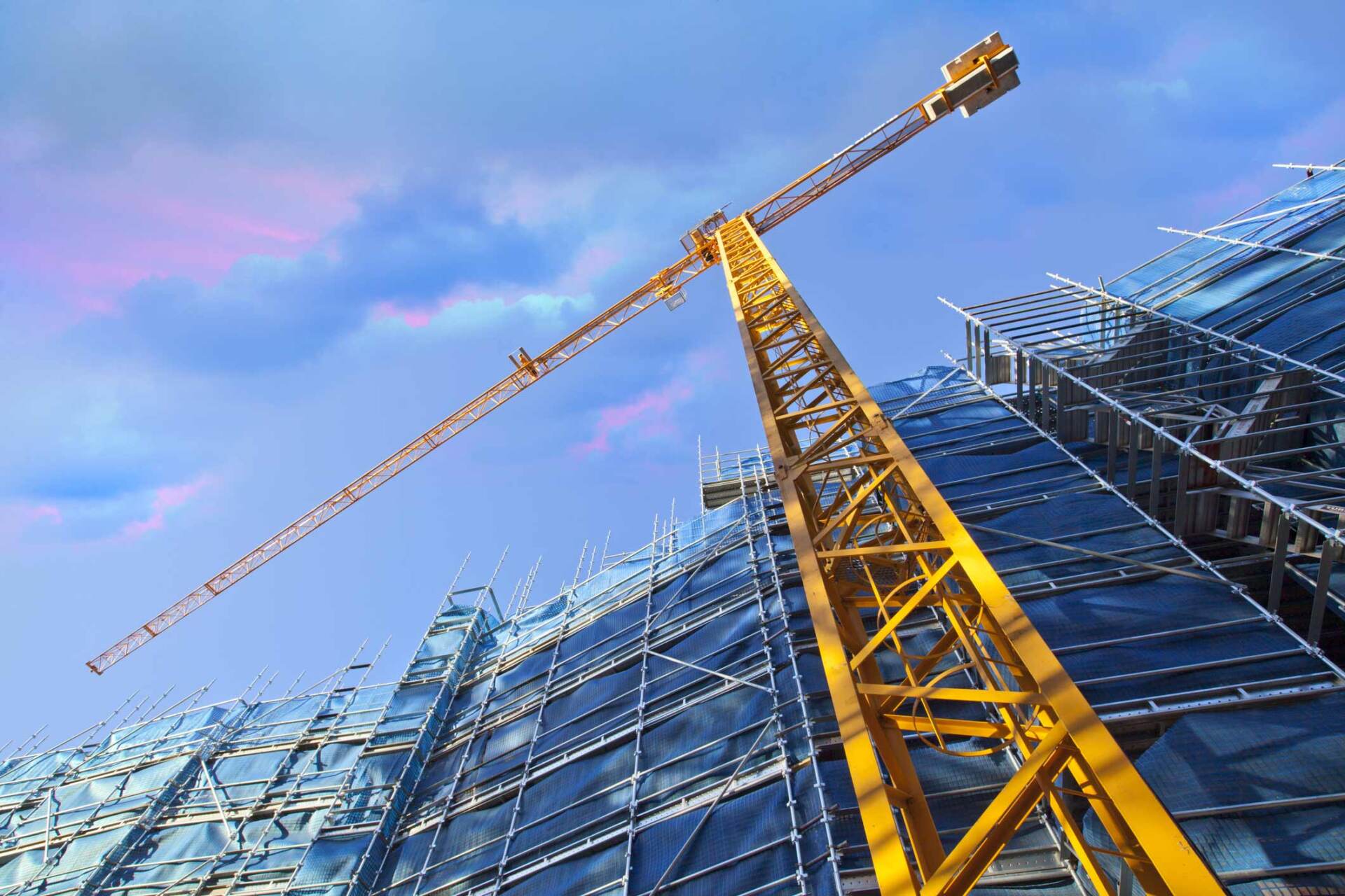 A yellow crane is sitting on top of a building under construction.