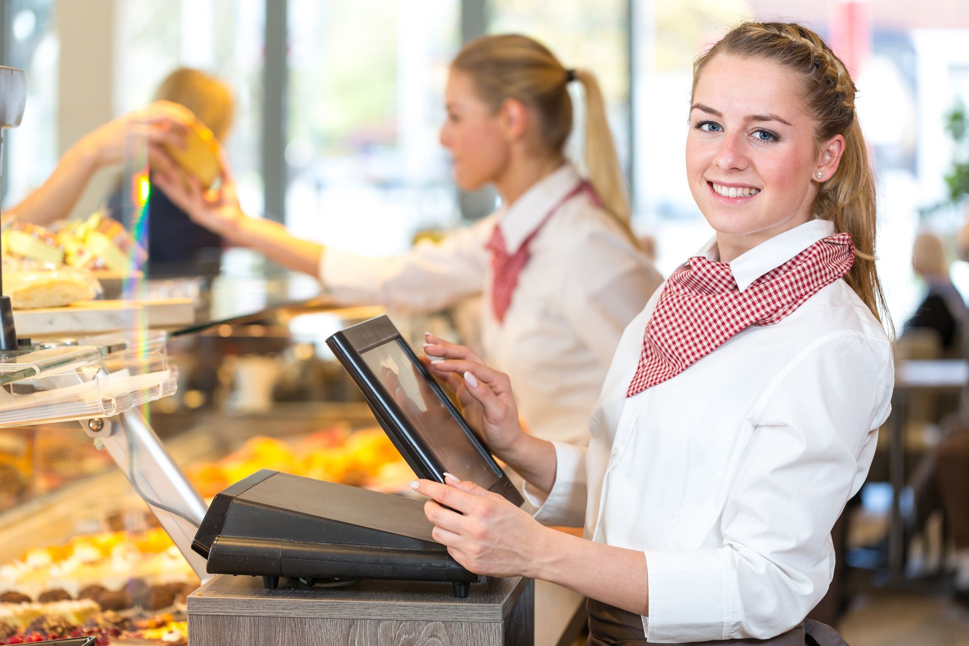 A woman is standing in front of a cash register in a bakery.