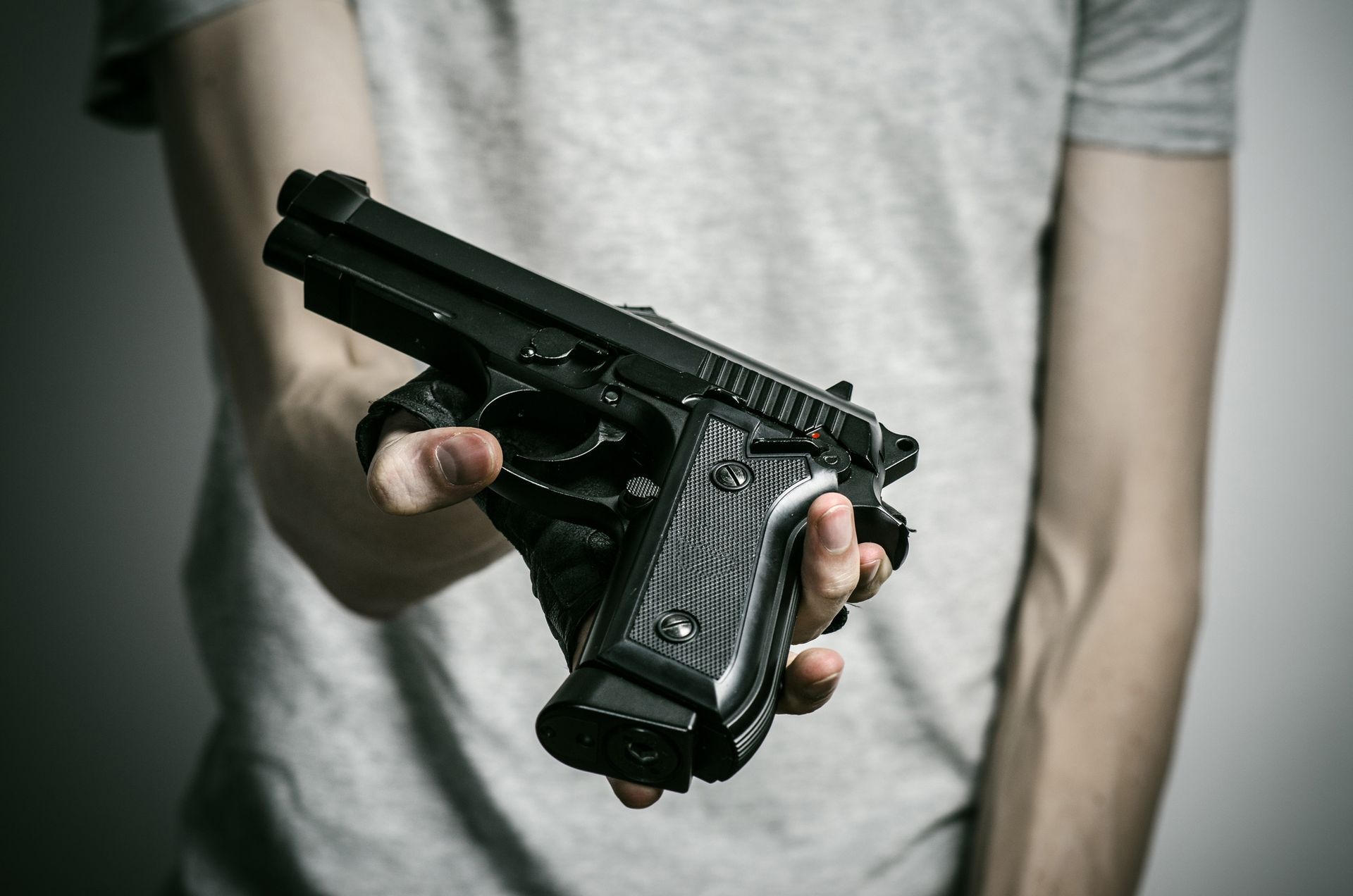 Person in grey shirt holding a black handgun, arm outstretched.