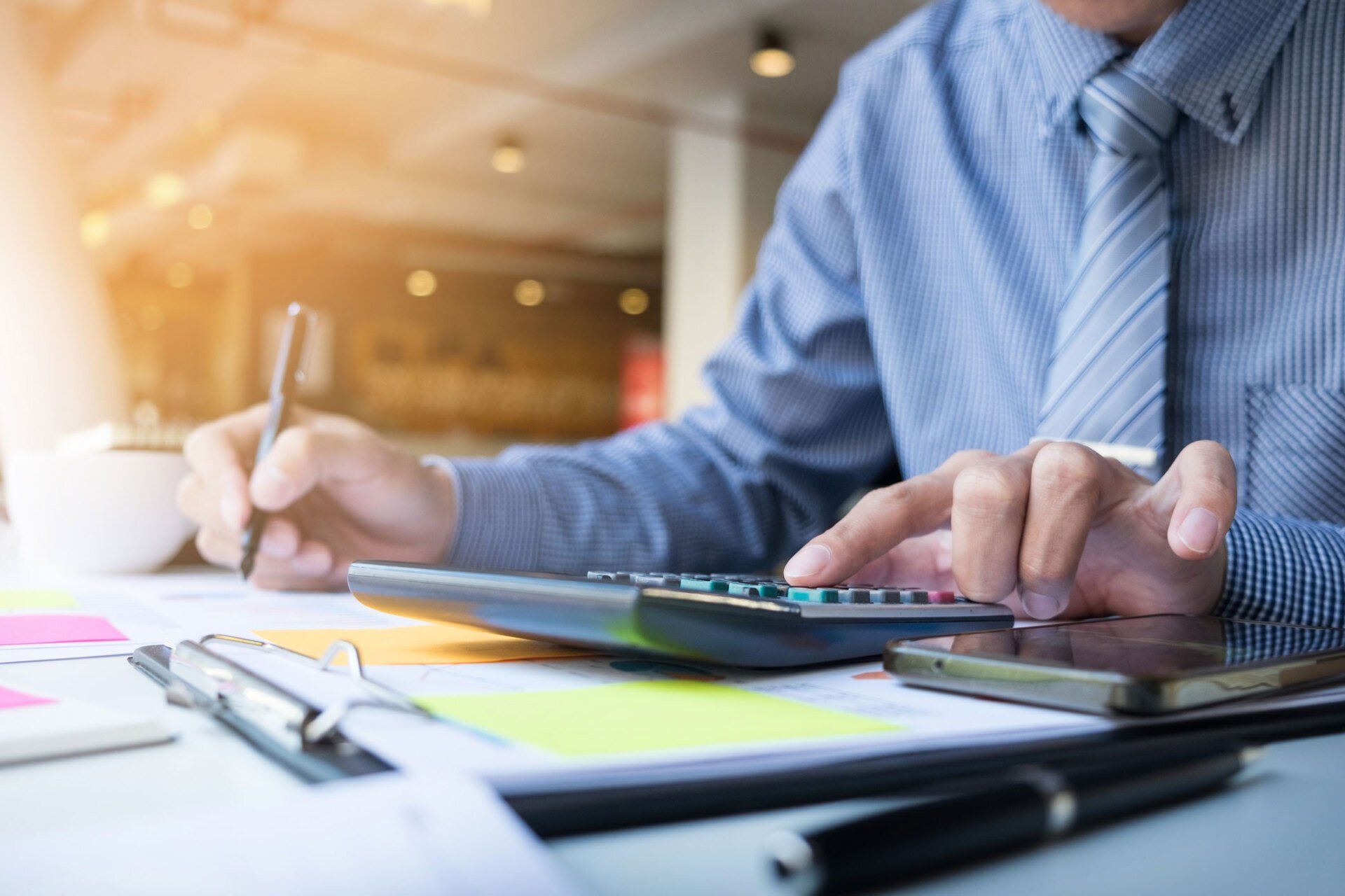 A man is sitting at a desk using a calculator and writing something down.