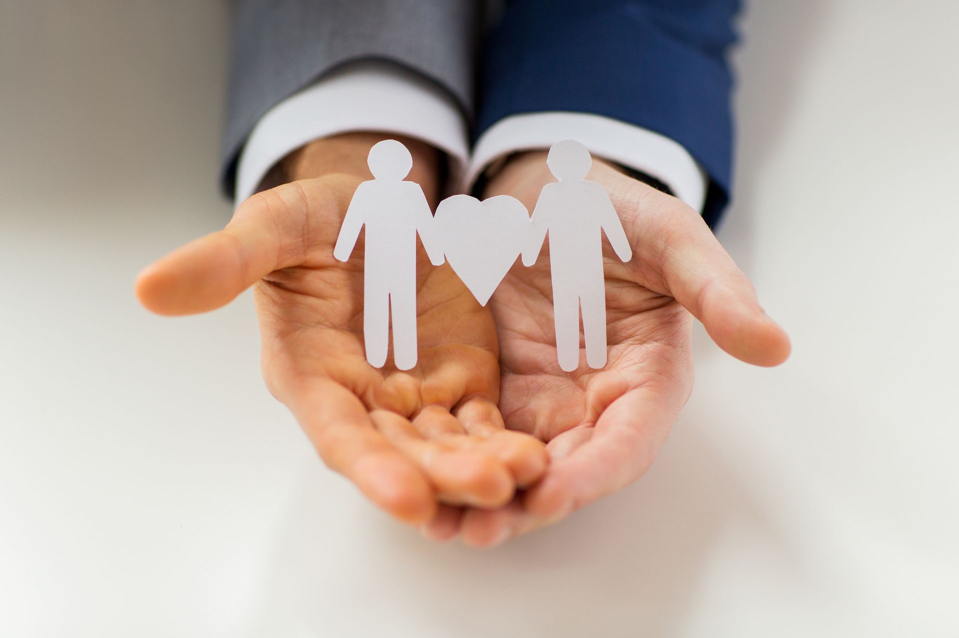 A person is holding two paper people and a heart in their hands.