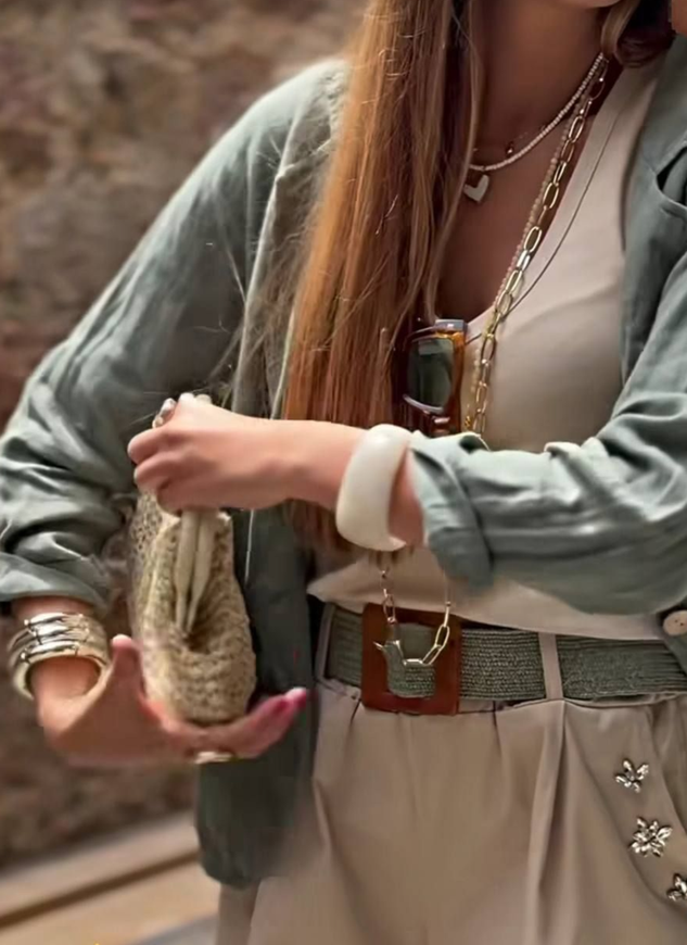 Donna in abito beige, con in mano una borsa. Giacca e cintura verdi. Lunghi capelli biondi.