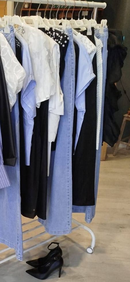Appendiabiti con vari top e jeans. Tacchi alti neri sul pavimento.