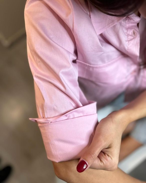 Donna con camicia rosa abbottonata, polsini alle maniche. Smalto rosso in mano.