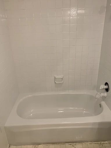 White bathroom with a built-in bathtub, tiled wall, and chrome faucet.