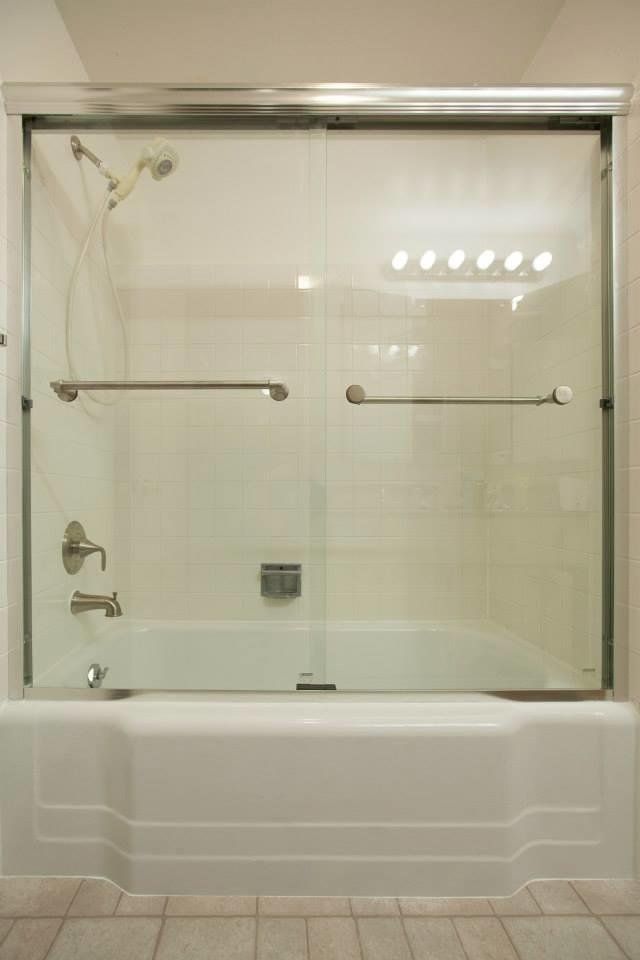 Bathtub with glass shower enclosure, white tile, and chrome grab bars in a bathroom