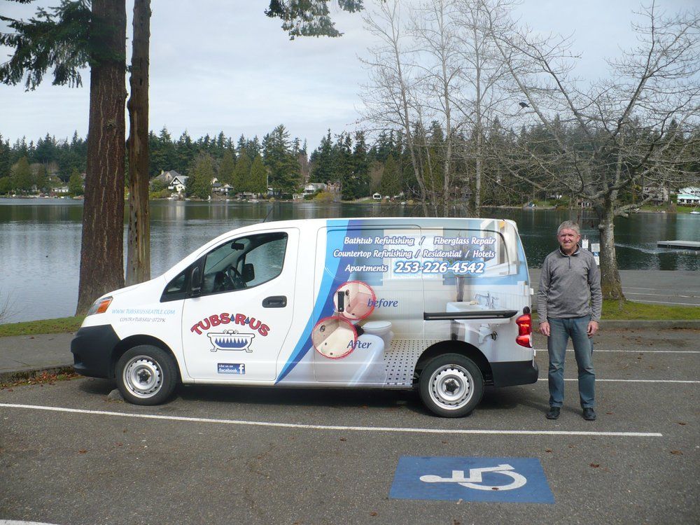 White advertising van parked by a lake, with a man standing beside it and a disabled parking space in front.