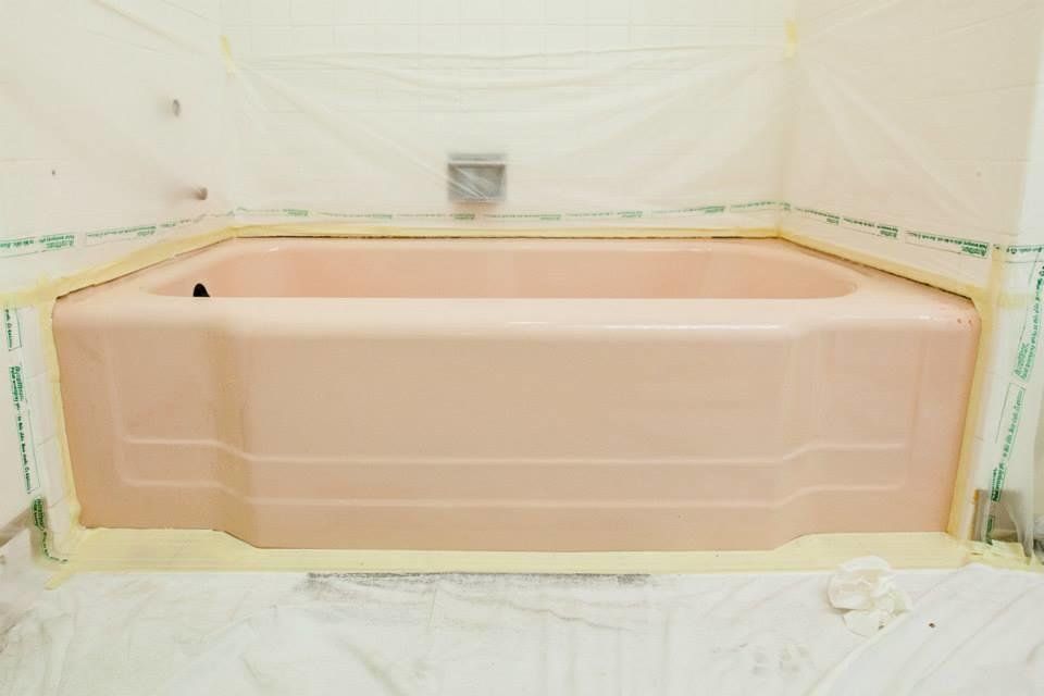 Pink bathtub in a bathroom under renovation, surrounded by protective plastic sheeting and tape