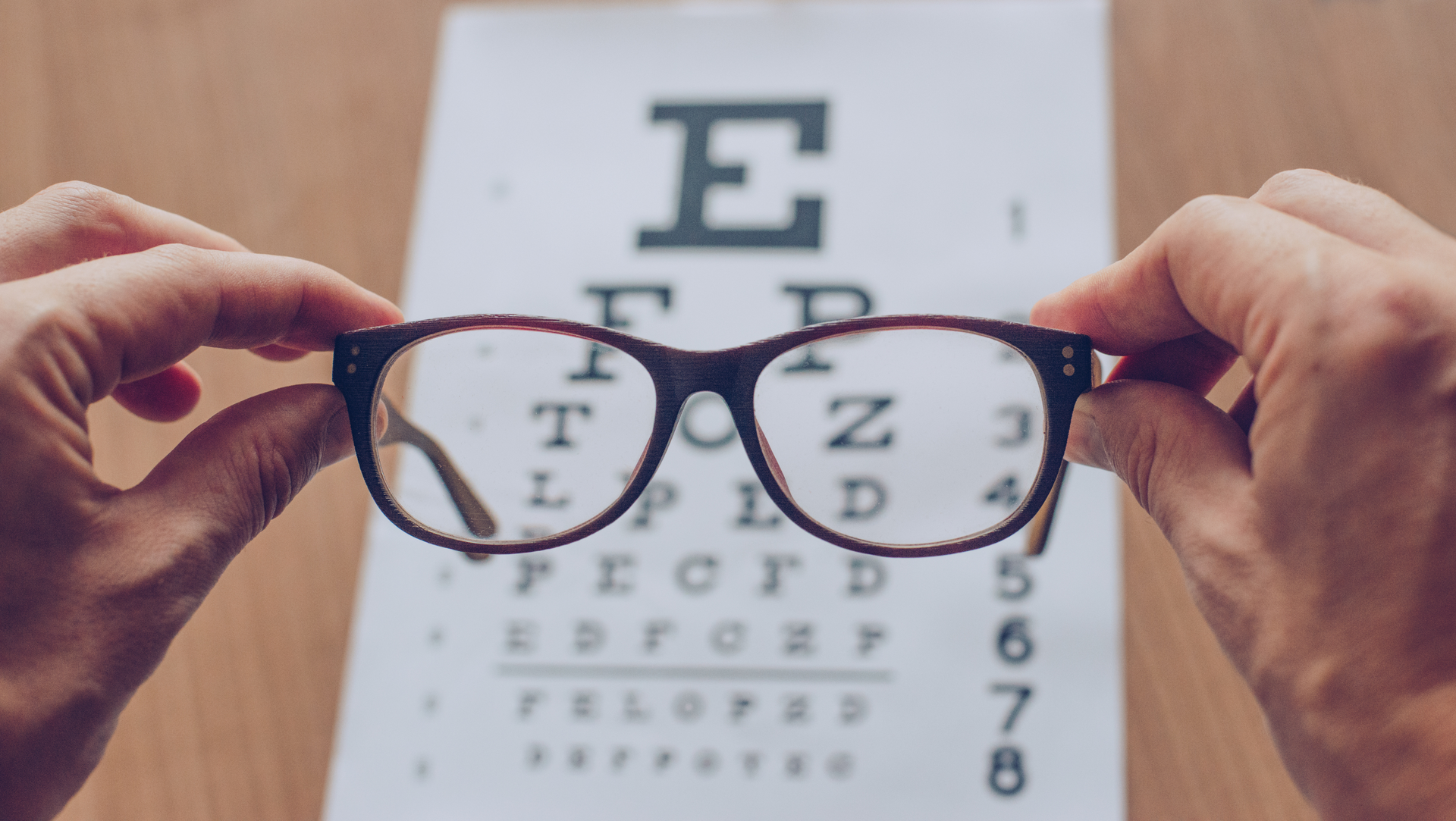 A person is holding a pair of glasses in front of an eye test chart.