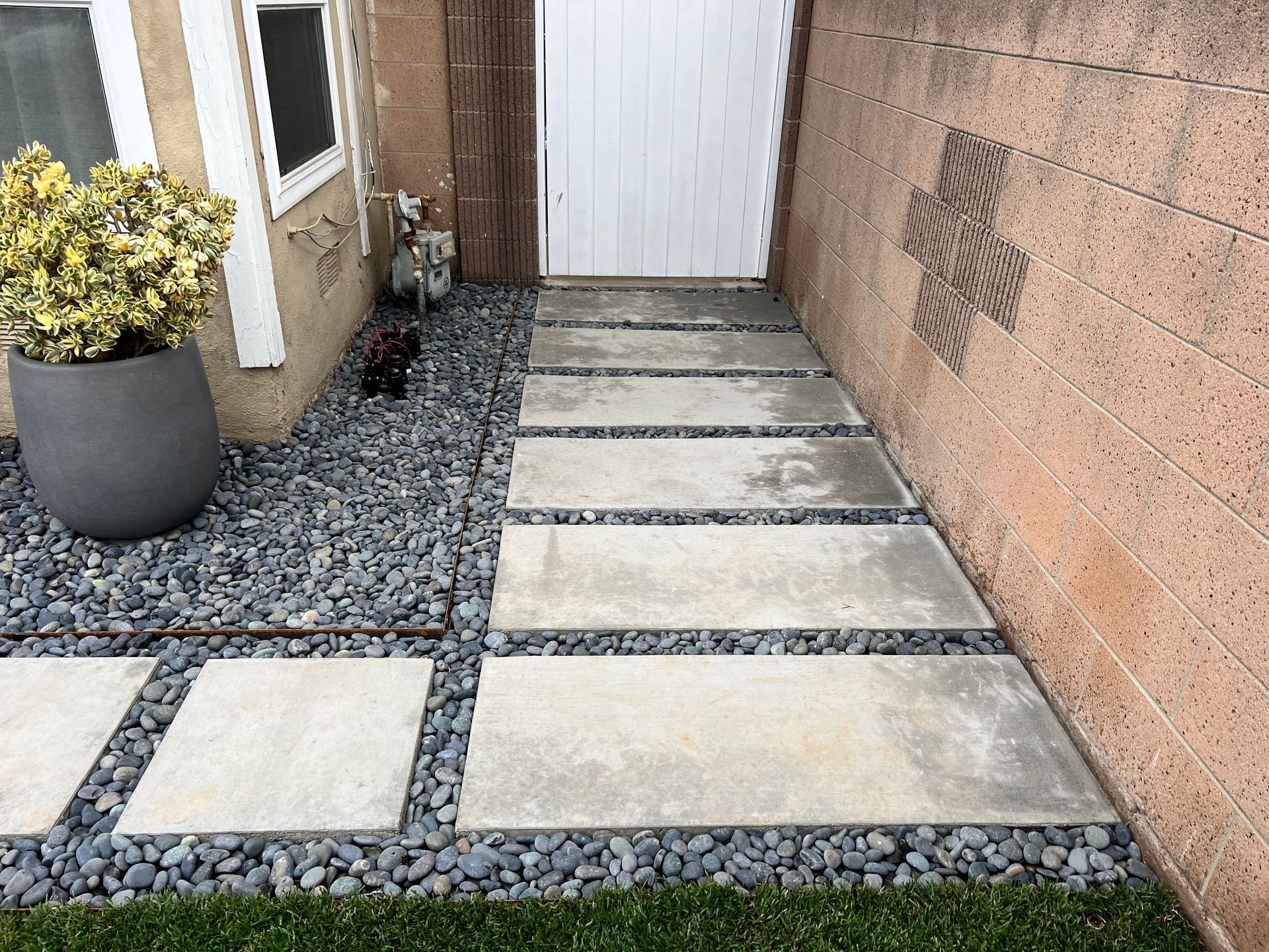 A stone walkway leading to a door with a potted plant in the background.