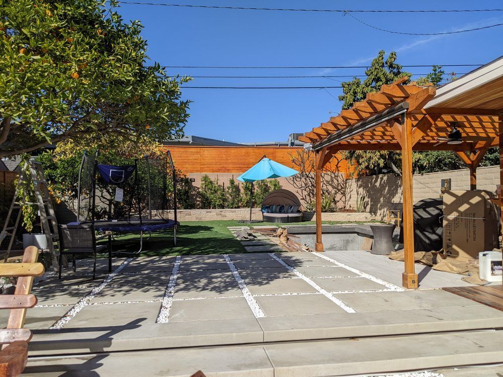 A backyard with a wooden pergola and a blue umbrella.