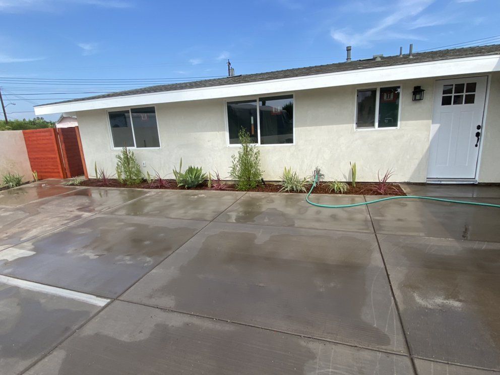 A white house with a concrete driveway and a hose in front of it.