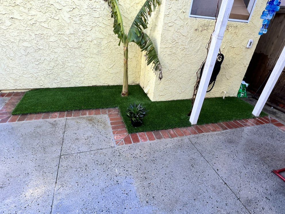 A concrete patio with artificial grass and brick borders