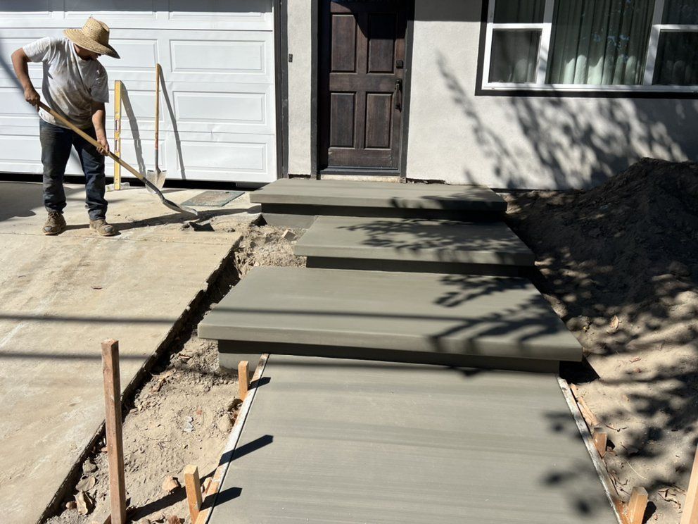 A man is working on a concrete walkway in front of a house