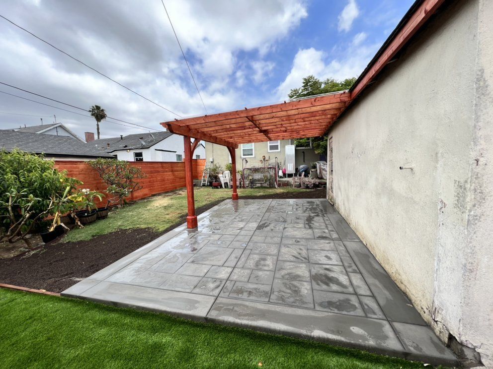 A backyard with a concrete patio and a wooden pergola.