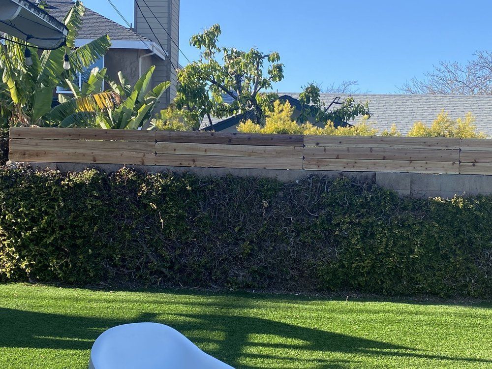 A white chair is sitting on a lush green lawn in front of a wooden fence.