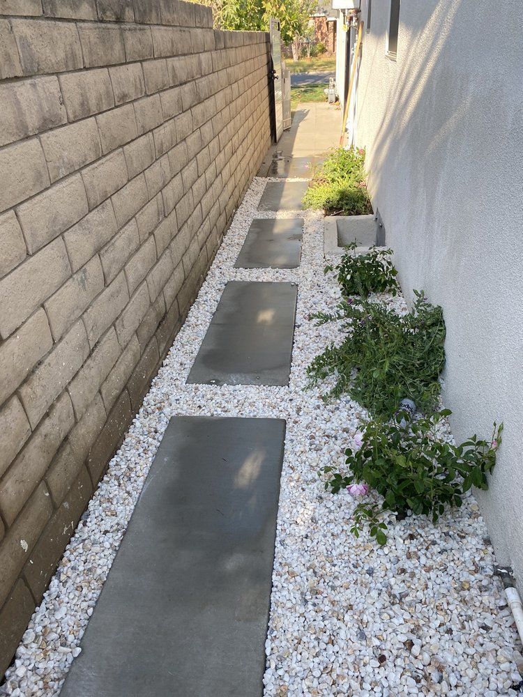 A sidewalk lined with white gravel and plants next to a brick wall.