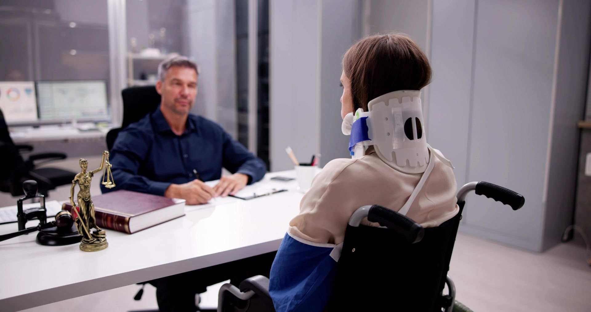 A woman in a wheelchair is sitting at a desk talking to a man.