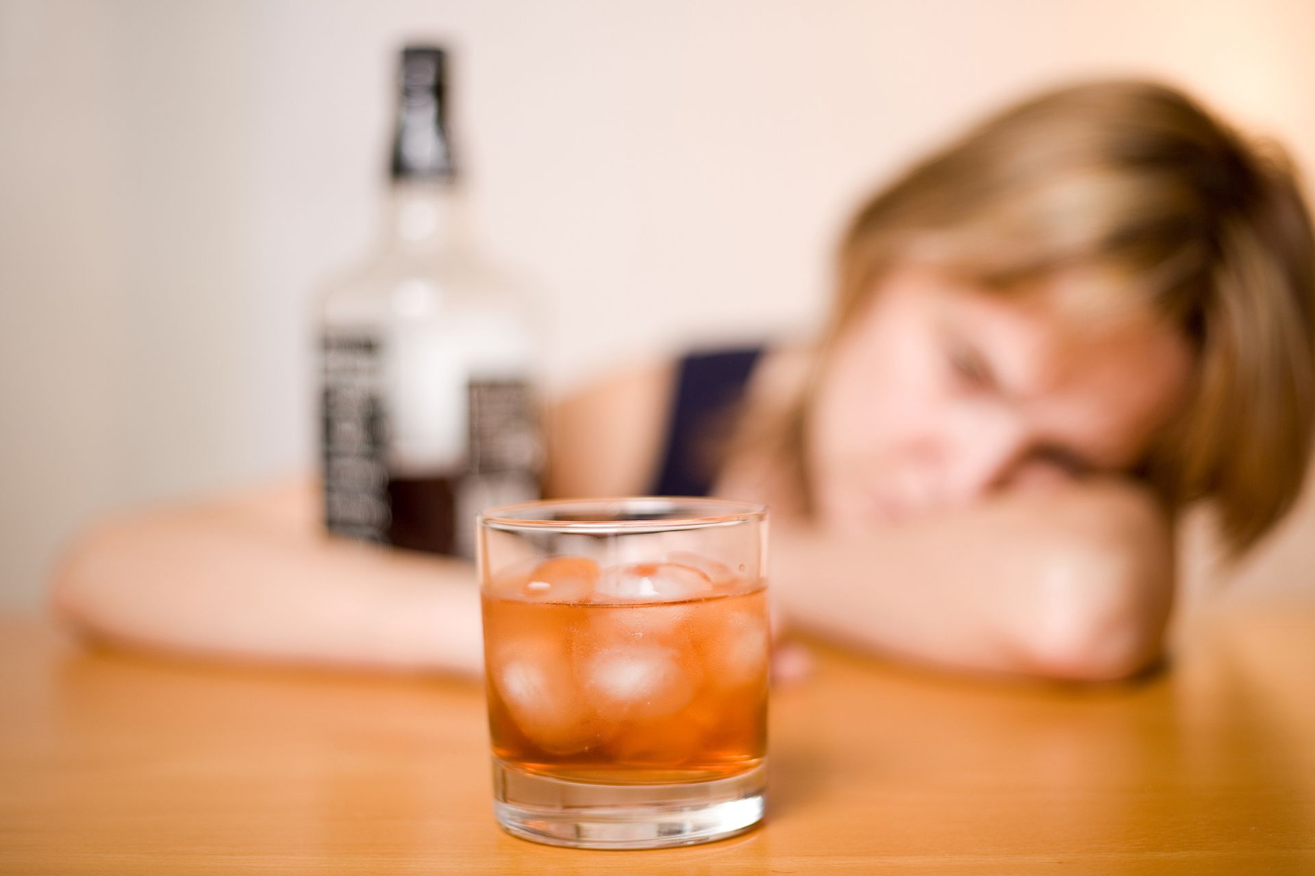 A woman is sitting at a table with a bottle of jack daniels and a glass of whiskey.
