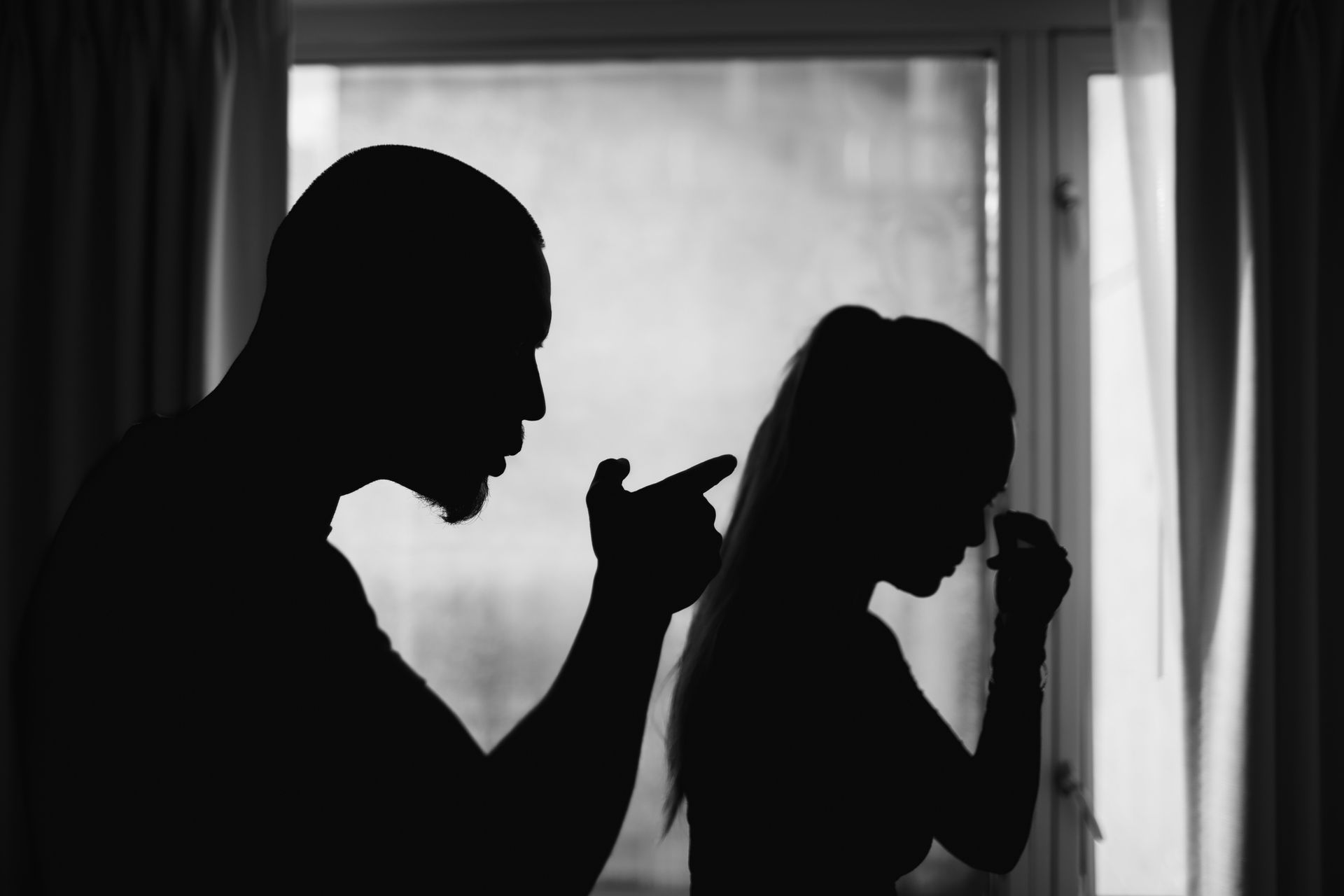 A man and a woman are having an argument in front of a window.