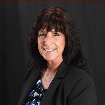 A woman wearing a black jacket and a blue and white shirt is smiling for the camera. A woman wearing a black jacket and a blue and white shirt is smiling for the camera.