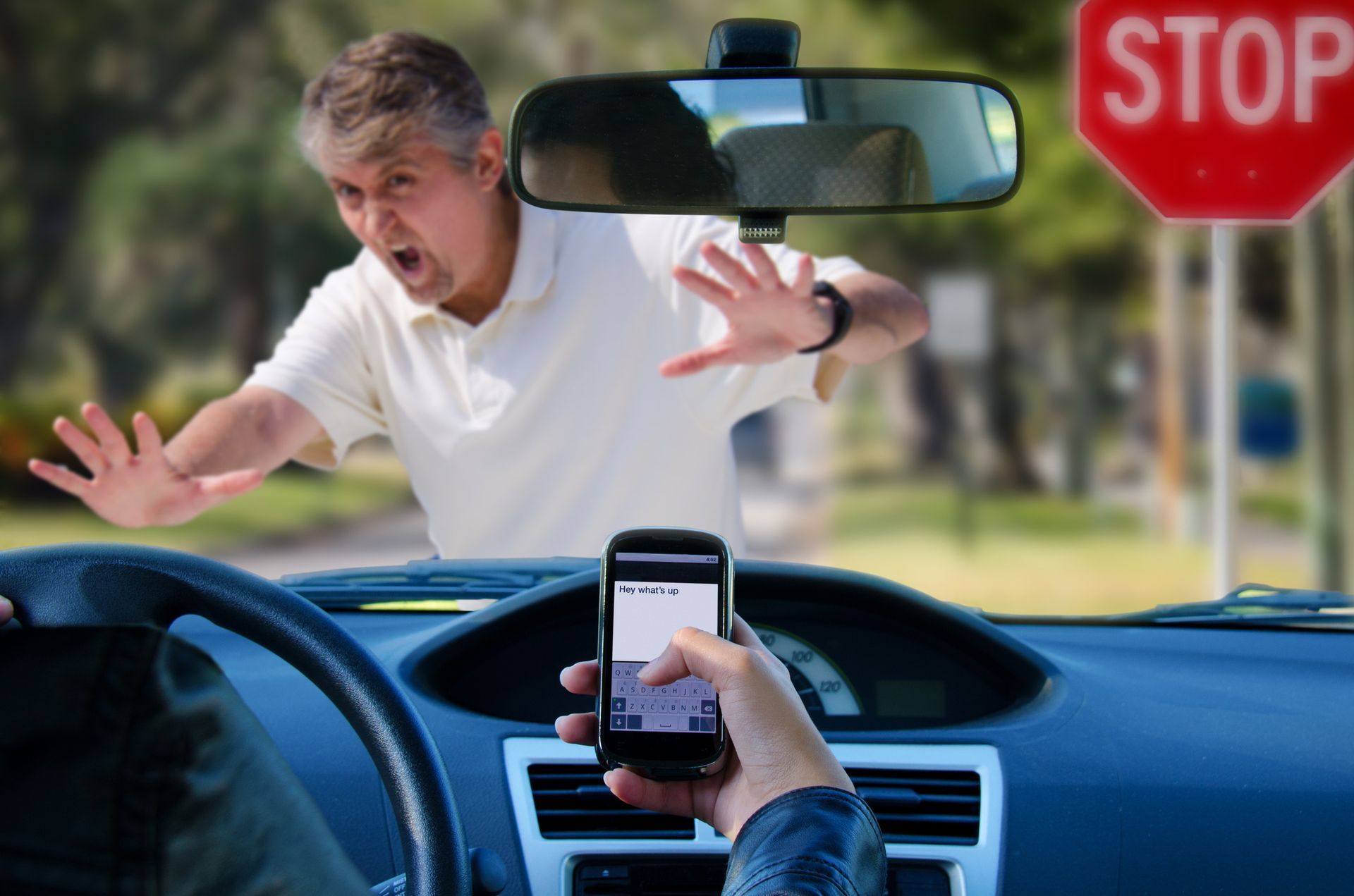 A person is holding a cell phone in front of a stop sign.