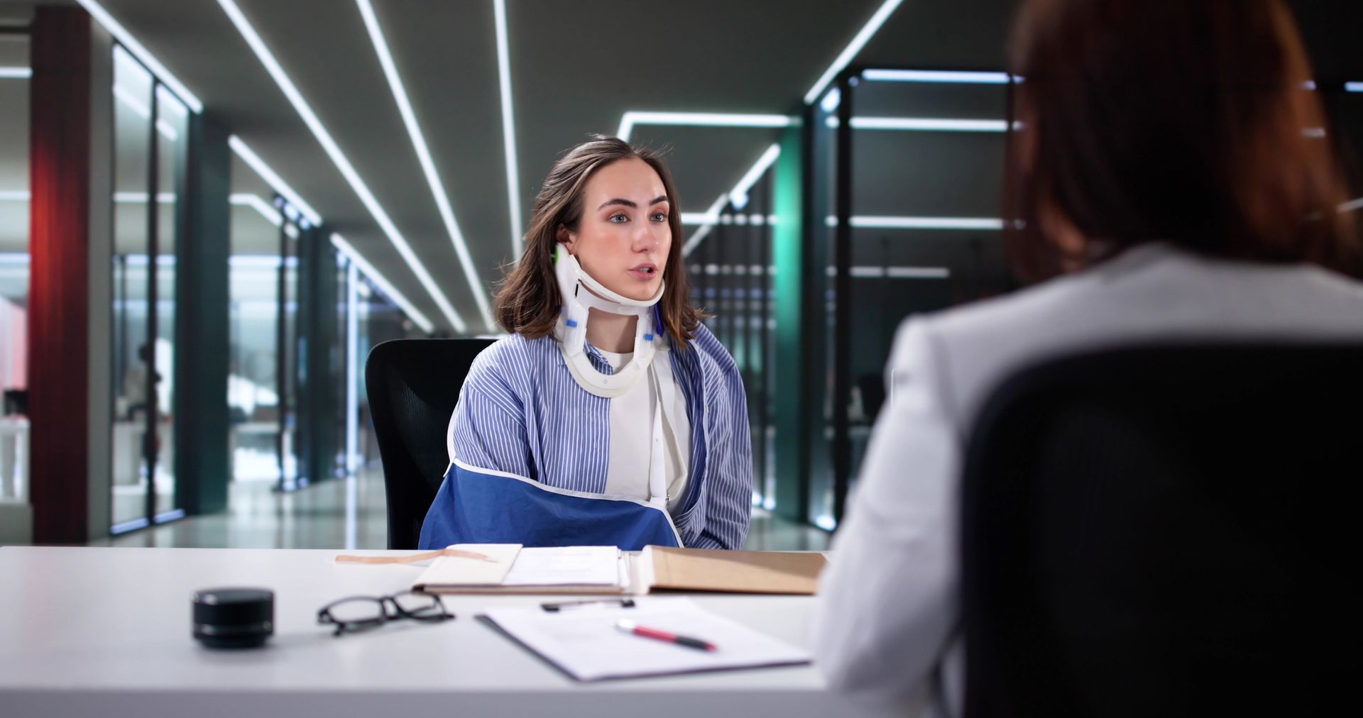 A woman with a broken arm is sitting at a desk talking to a doctor.