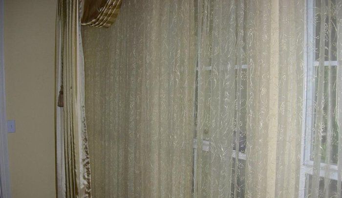 Sheer beige curtains in front of a window, allowing light to filter through.  A decorative valance is above.