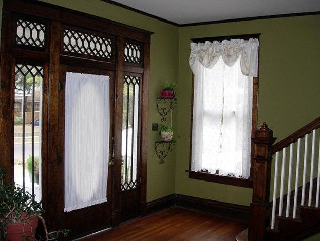 An entryway with a dark wood door and trim, a window with a white curtain, and a staircase. The walls are painted green.