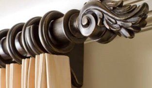 Ornate bronze curtain rod with decorative leaf end, holding beige curtains.