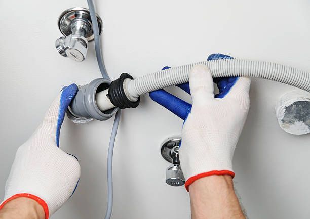 Workman with white gloves attaches a hose to a drain sewage pipe.