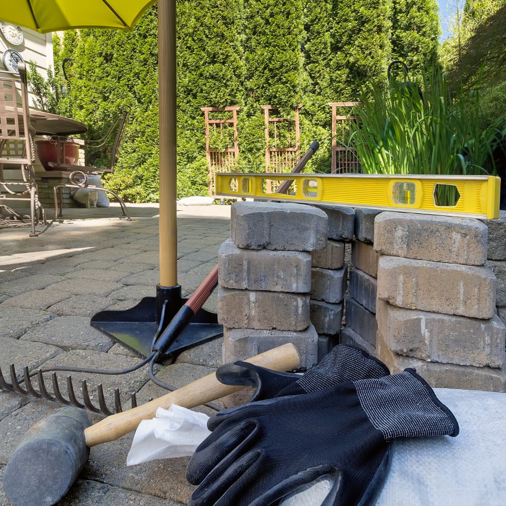 Construction scene with bricks, tools, level, and gloves on a patio.