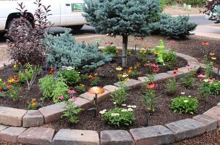 Circular garden bed with colorful flowers and shrubs framed by brick edging.