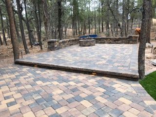 Stone patio with raised section, fire pit, and surrounding trees.
