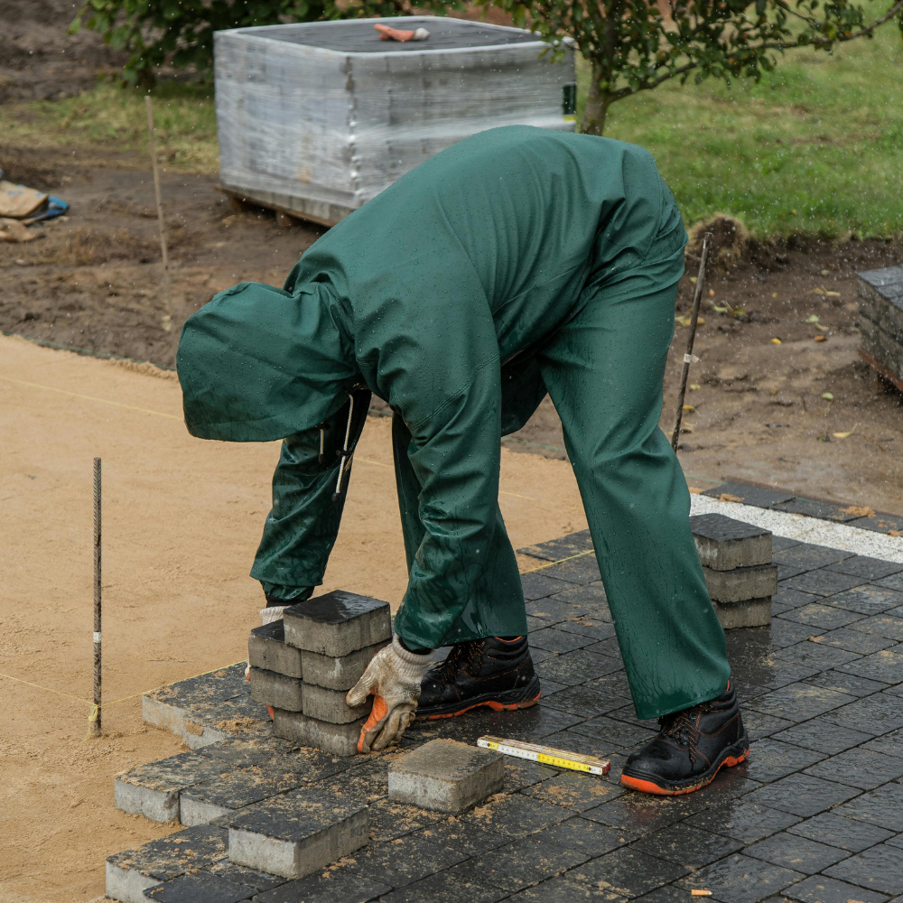 Person in green work suit laying paving stones.