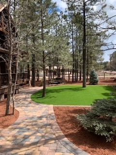 Stone pathway curves through a green lawn, leading to a wooden building in a wooded setting.