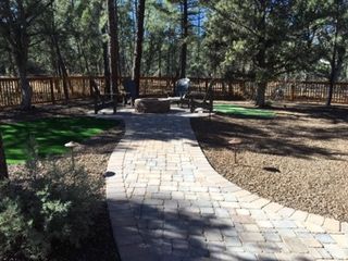 Stone path leads to a fire pit with chairs in a backyard with trees and grass.