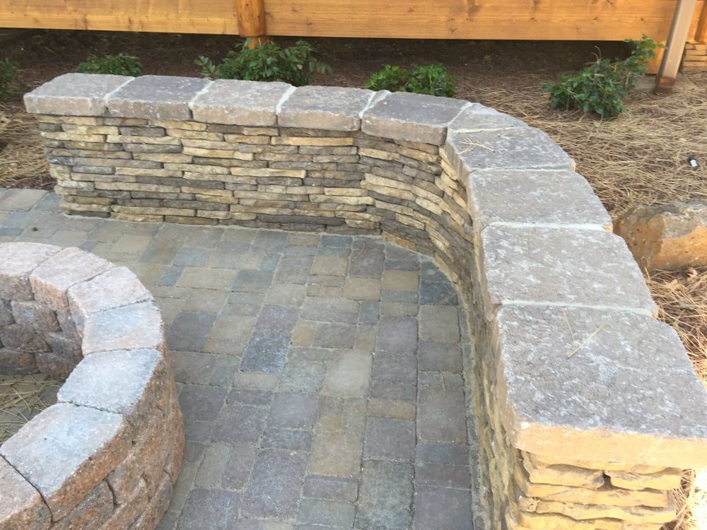 Curved stone retaining wall with matching pavers, and fire pit in outdoor setting.