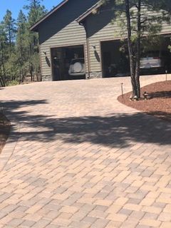 Paved driveway leading to a two-car garage with visible vehicles inside. Green siding, brown trim, and surrounding trees.