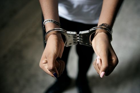 Hands in handcuffs. Arms are outstretched in front of a person against a textured surface.