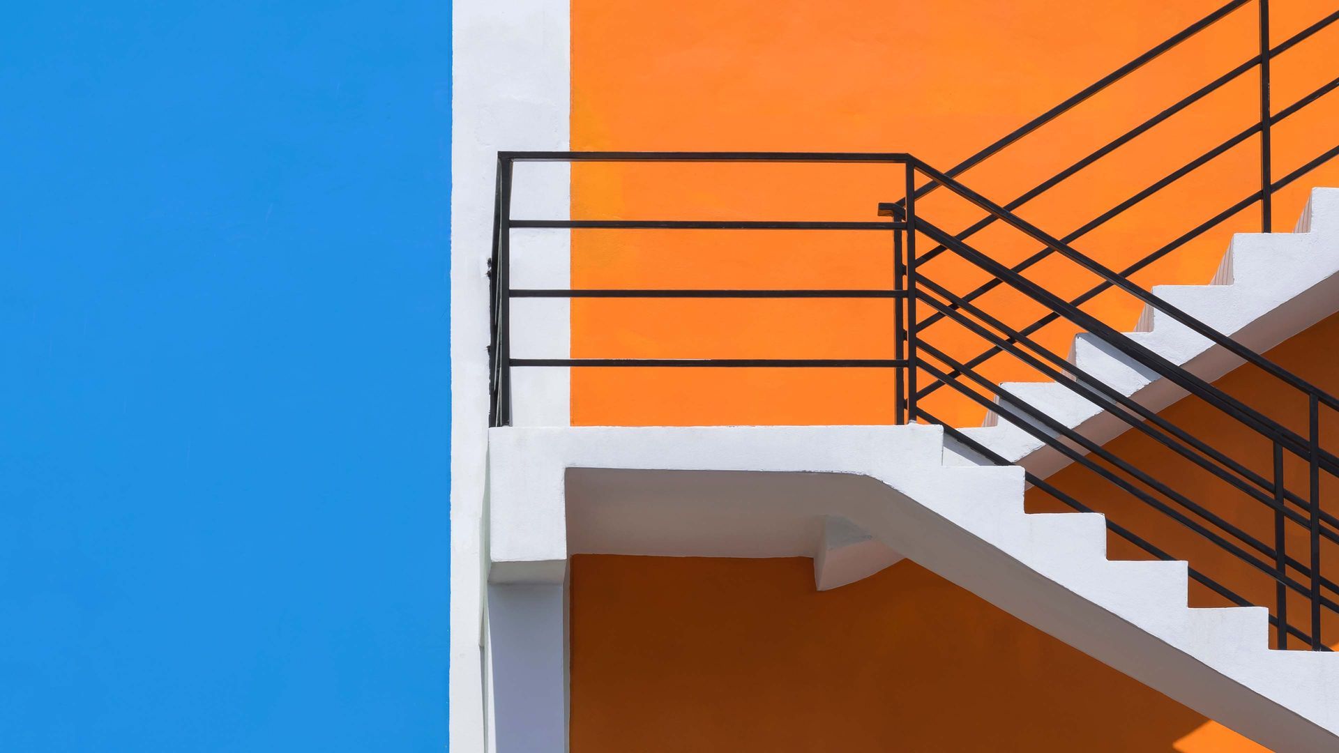 Orange building exterior with white stairs and black railing against a blue sky.