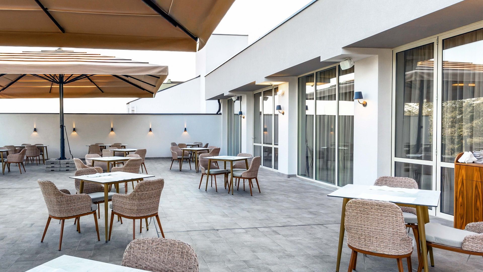 Outdoor patio with tables and chairs, under a large umbrella, beside a white building with windows.