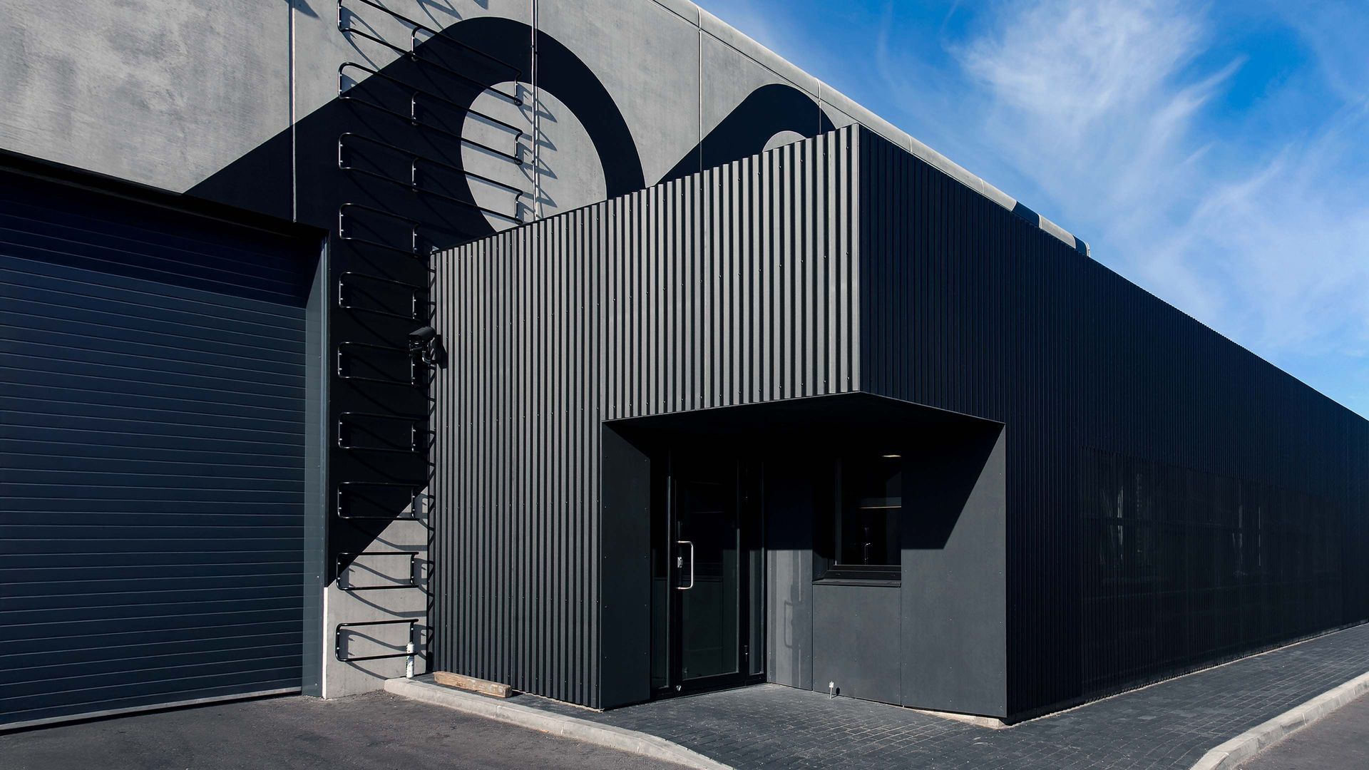 Modern commercial building with dark metal cladding and glass entrance under blue sky
