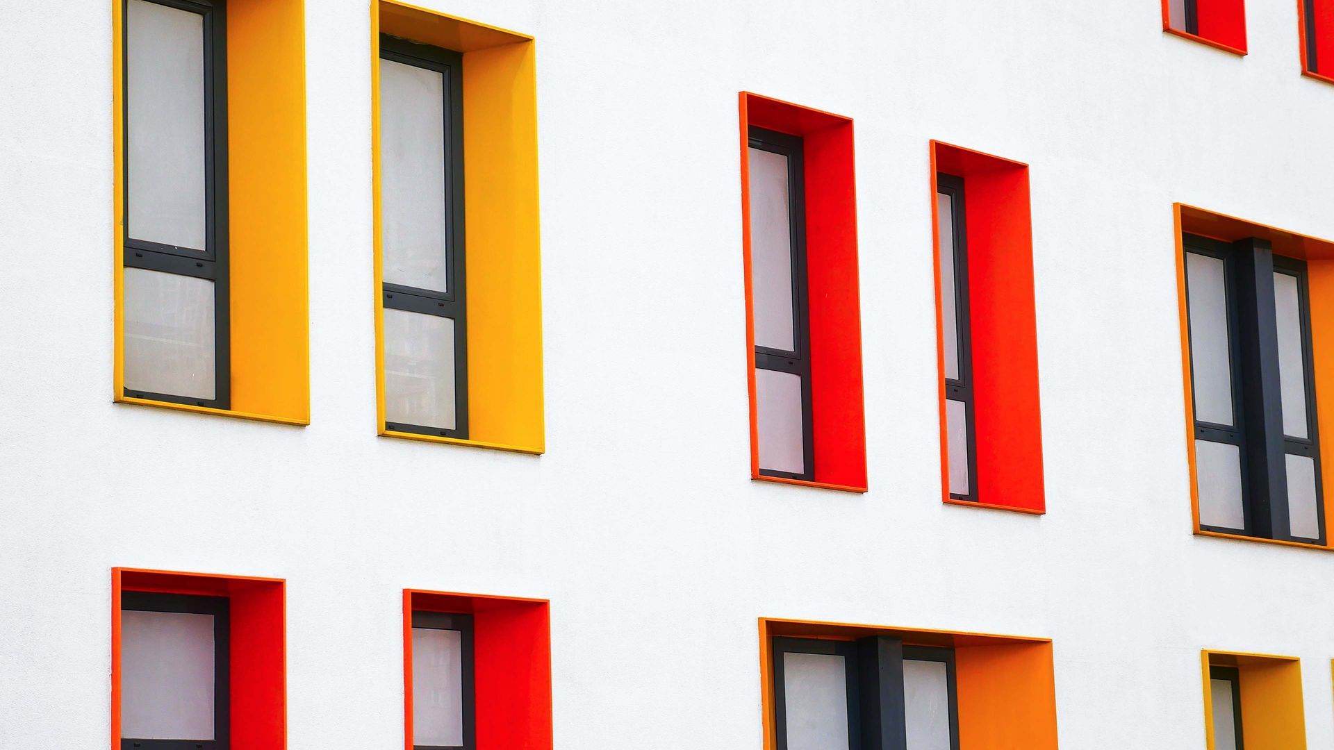 White building facade with rows of windows framed in orange and yellow.