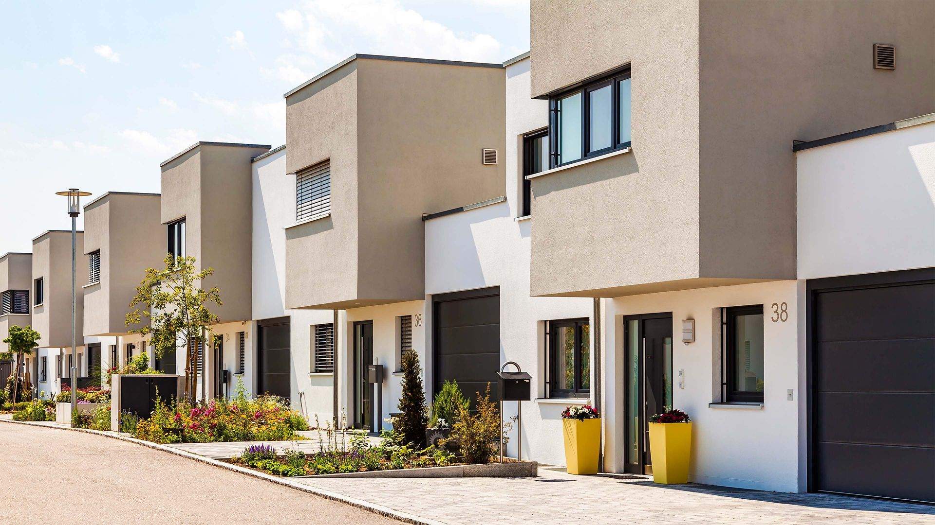 Row of modern townhouses, gray and white with black windows and doors, sunny day.
