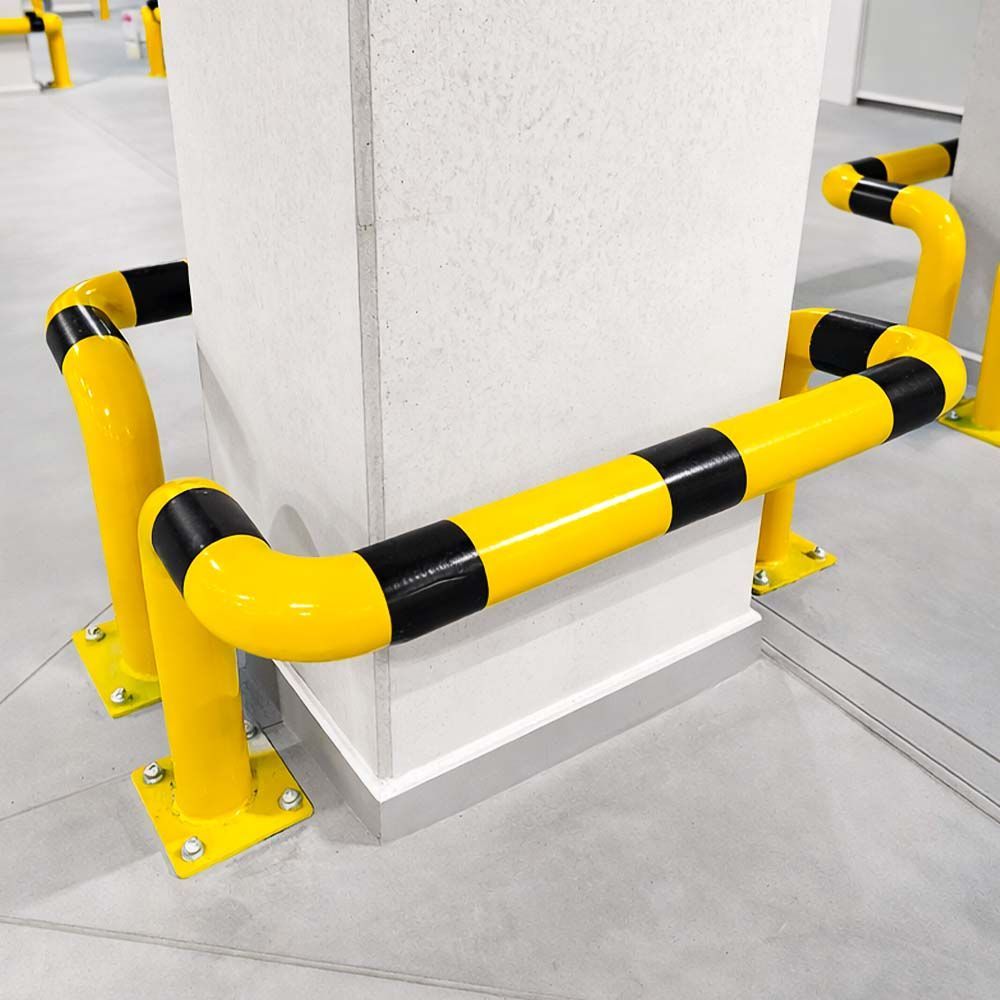 Yellow and black protective barriers around a white concrete pillar in a parking garage.